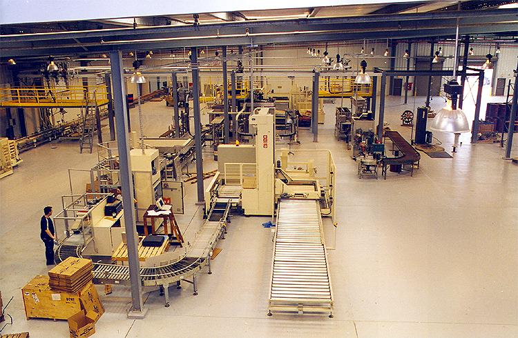 Wide view of a manufacturing plant with conveyor belts, large machinery, and a worker at a workstation.
