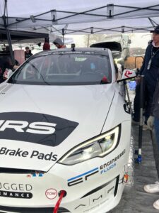 White race car under a canopy in a pit area, front shot with sponsor logos and a red tow hook.