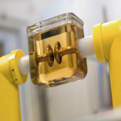 Close-up of a transparent glass chamber with a rotating rotor inside, held by yellow laboratory clamps.