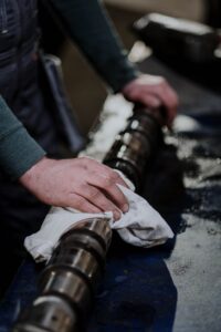 Hands wrap a white cloth around a large metal shaft in a workshop, with a blurred background.
