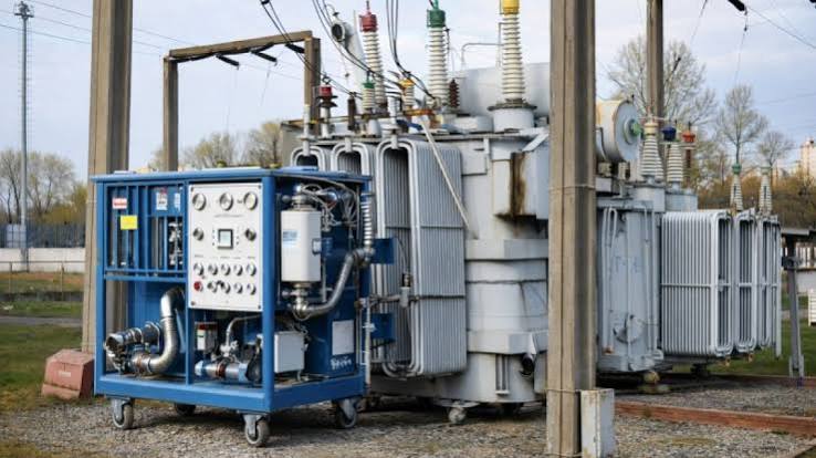 Outdoor electrical substation with large transformers and high-voltage insulators; a blue maintenance generator panel sits in front.